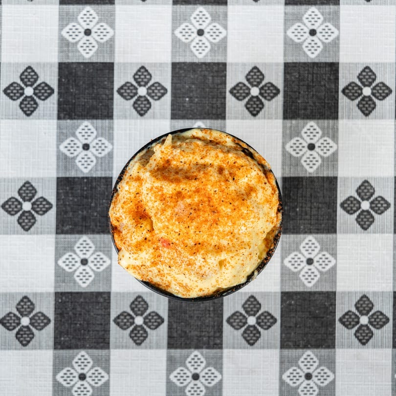 Overhead view of a creamy dish with orange seasoning, on a black and white checkered tablecloth.