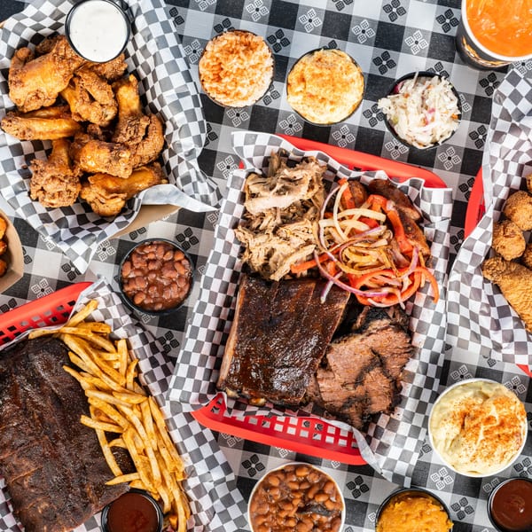 Overhead view of a barbecue feast with ribs, brisket, pulled pork, wings, fries, and sides.