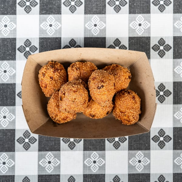 Golden-brown hushpuppies in a cardboard tray on a black and white checkered tablecloth.