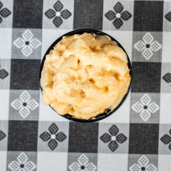 Creamy mac and cheese in a black bowl on a black and white checkered tablecloth.
