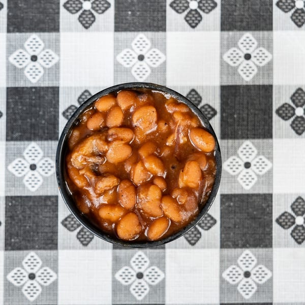 Overhead view of a black bowl filled with baked beans on a black and white checkered tablecloth.