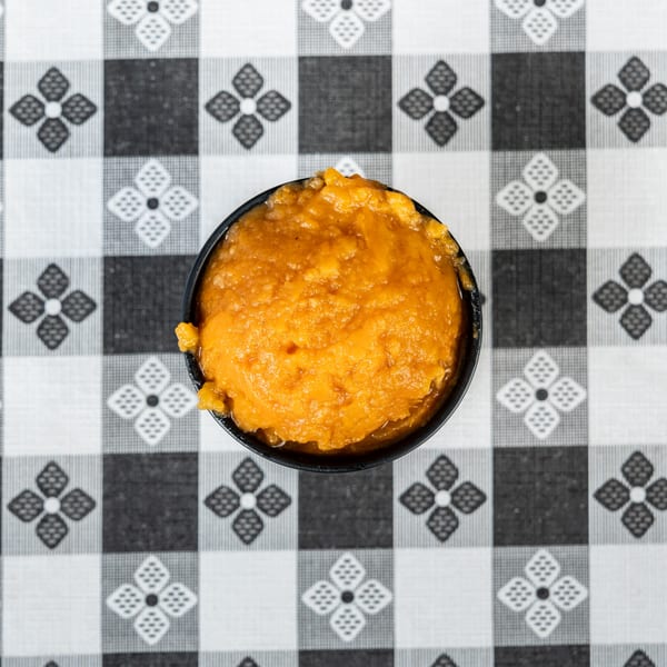 Overhead view of a small black bowl filled with orange mashed sweet potatoes on a checkered tablecloth.