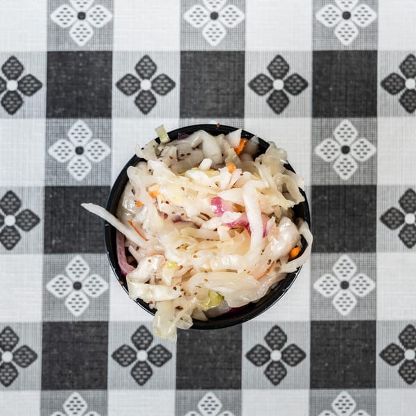 Overhead view of a small black bowl of coleslaw on a black and white checkered tablecloth.