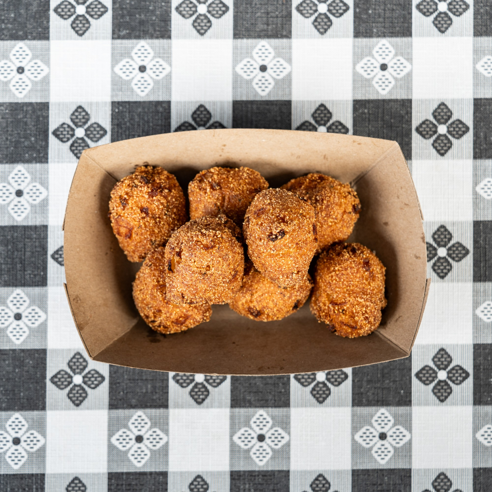 Hush puppies in a brown paper tray on a black and white checkered tablecloth.