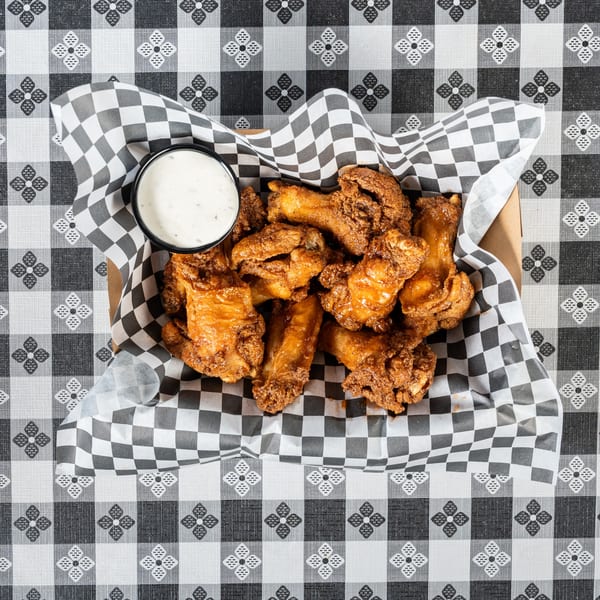 Crispy fried chicken wings with a side of ranch dressing in a checkered paper-lined basket.
