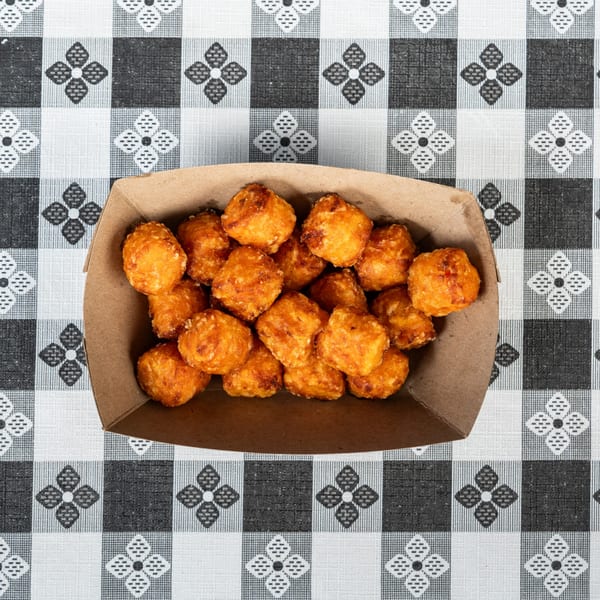 Golden brown fried cheese curds in a brown paper tray on a black and white checkered tablecloth.