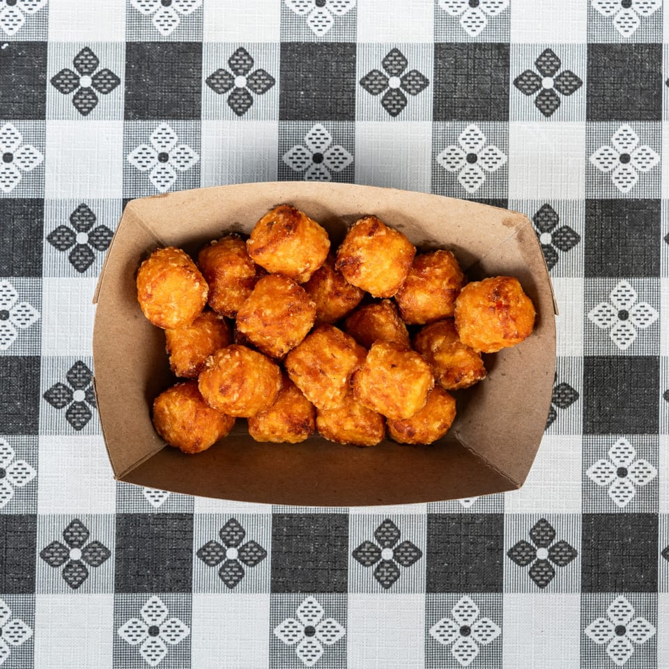 Golden brown fried cheese curds in a brown paper tray on a black and white checkered tablecloth.