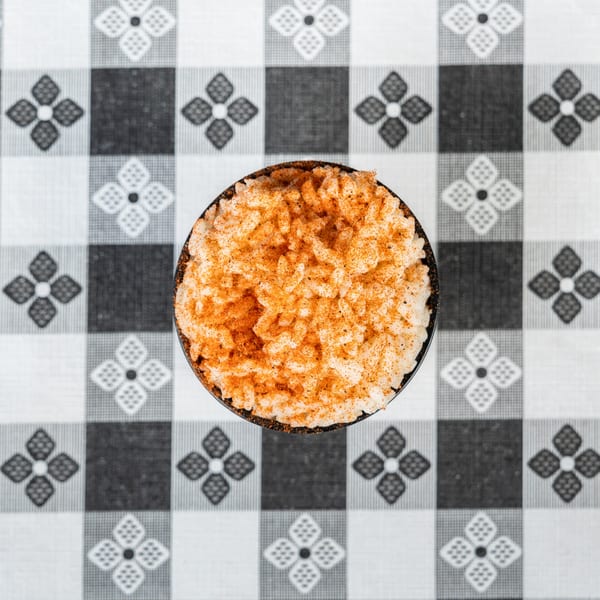 Overhead view of a bowl of rice with orange seasoning, on a black and white checkered tablecloth.