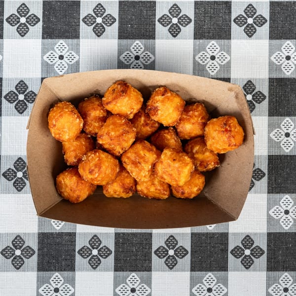 Golden brown tater tots in a cardboard tray on a black and white checkered tablecloth.