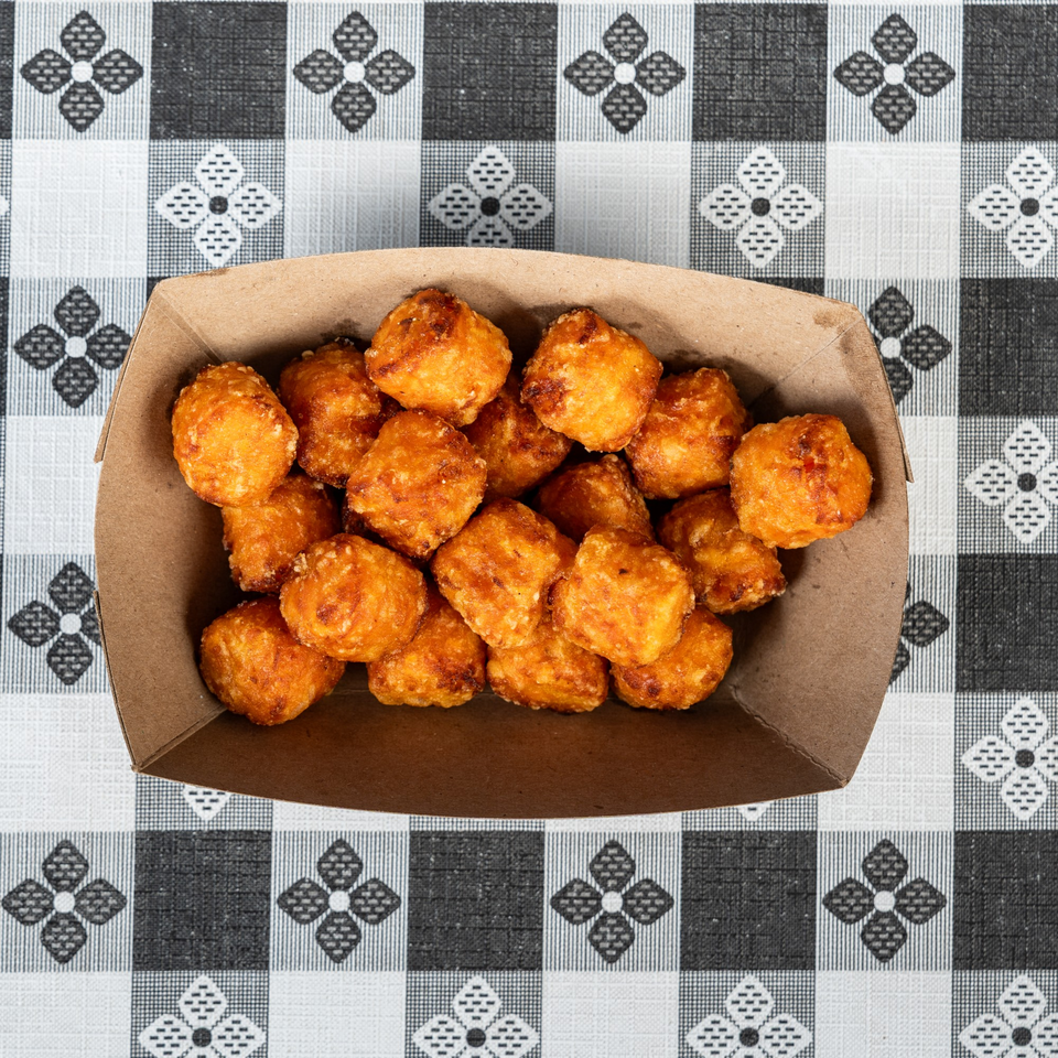 Golden brown tater tots in a cardboard tray on a black and white checkered tablecloth.